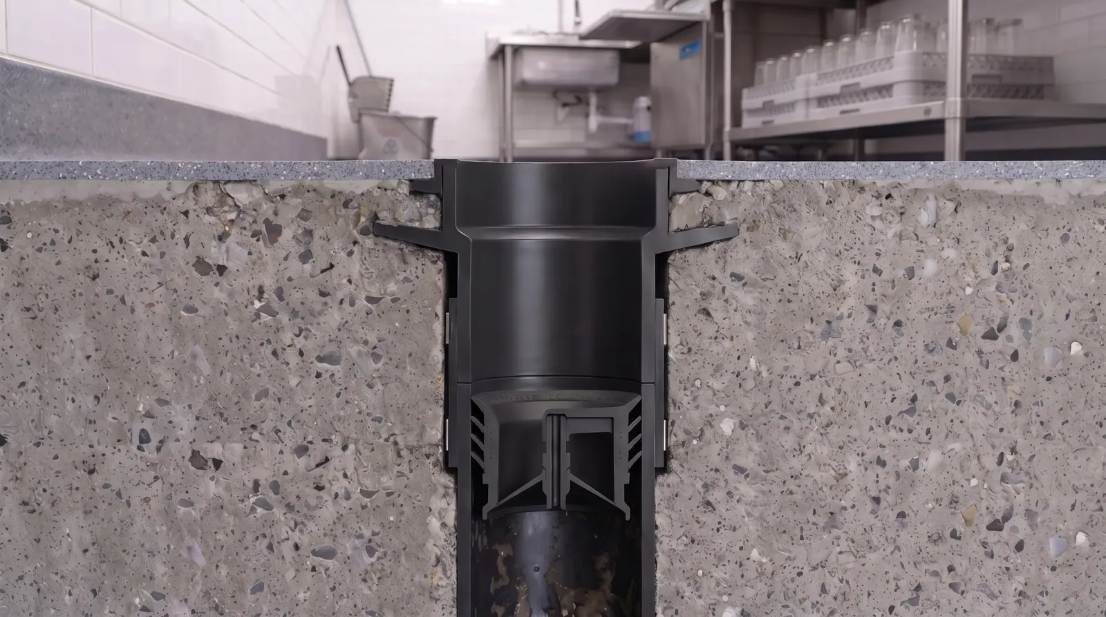 Cutaway of a commercial kitchen floor drain with a Green Drain waterless trap seal seated in the drain pipe below the floor